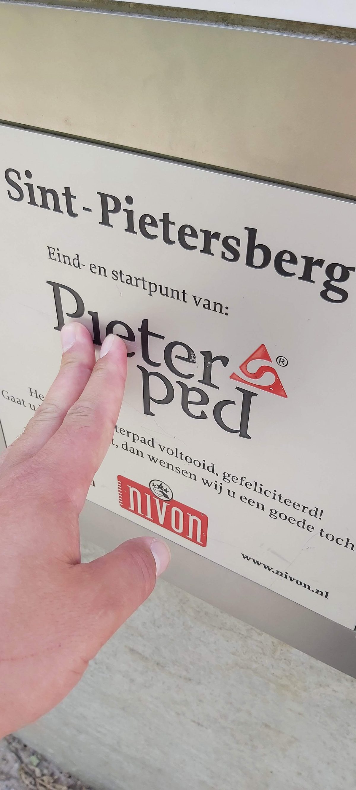 A hand touching the Pieterpad end marker at the Sint-Pietersberg in Maastricht