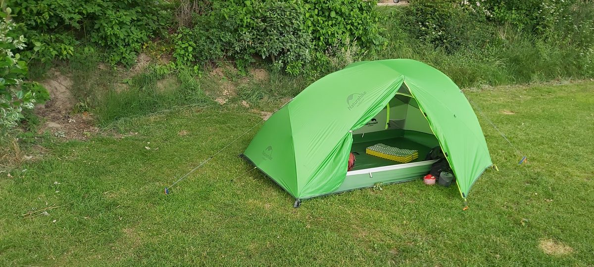 A small green trekking tent pitched on grass at a campsite on the Pieterpad