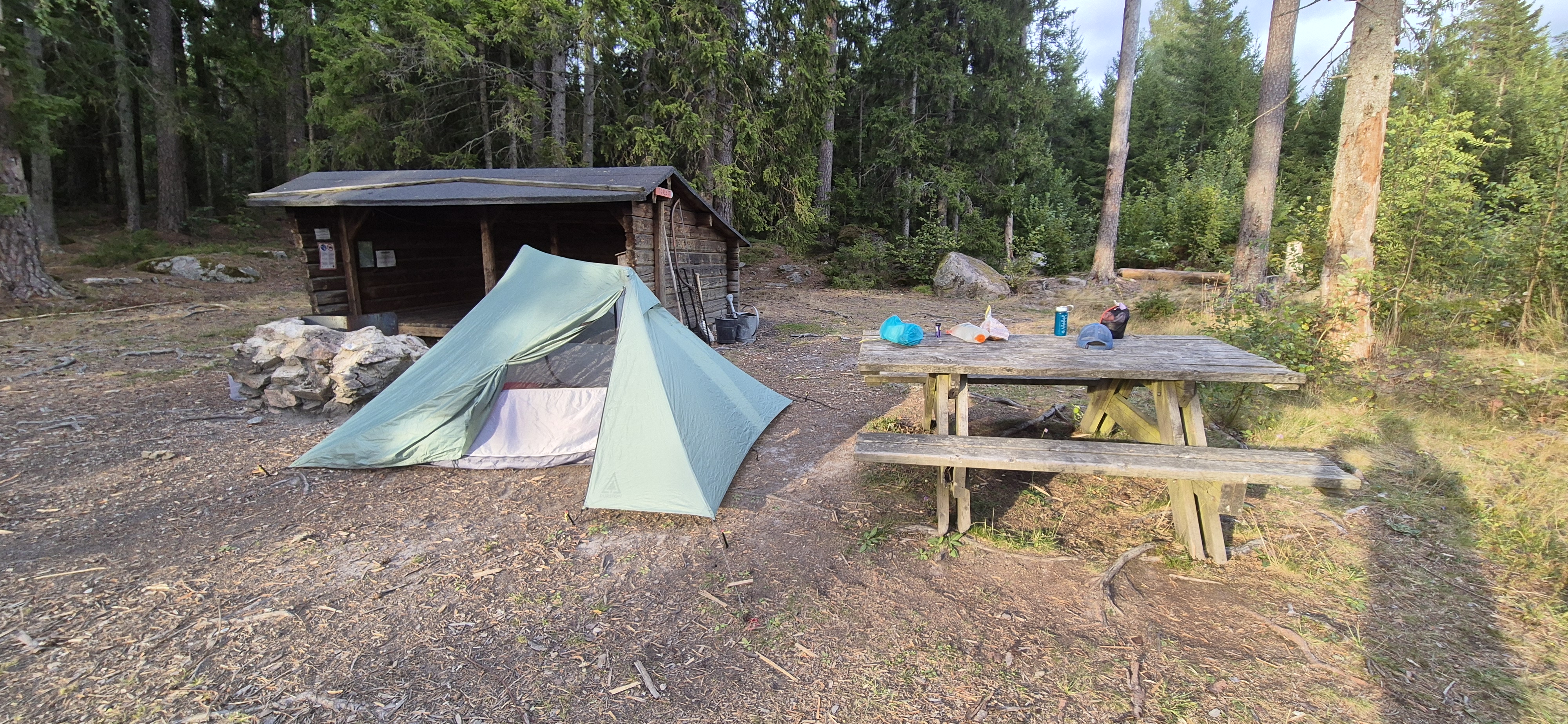 Green tent pitched next to a wooden log hut in the forest