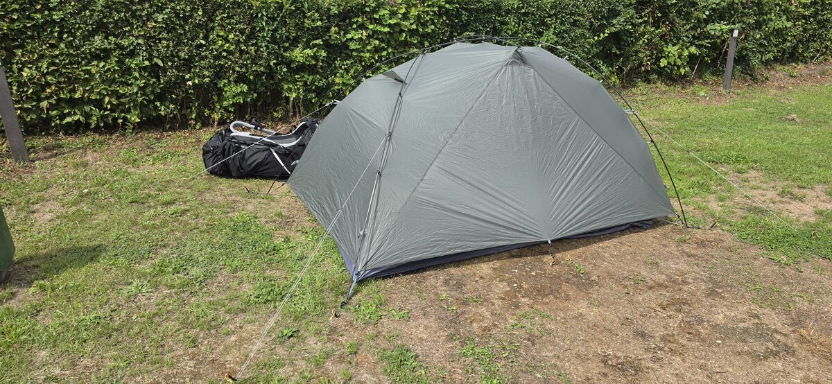 Tent pitched on grass with a backpack beside it at Camping Cottesserhoeve
