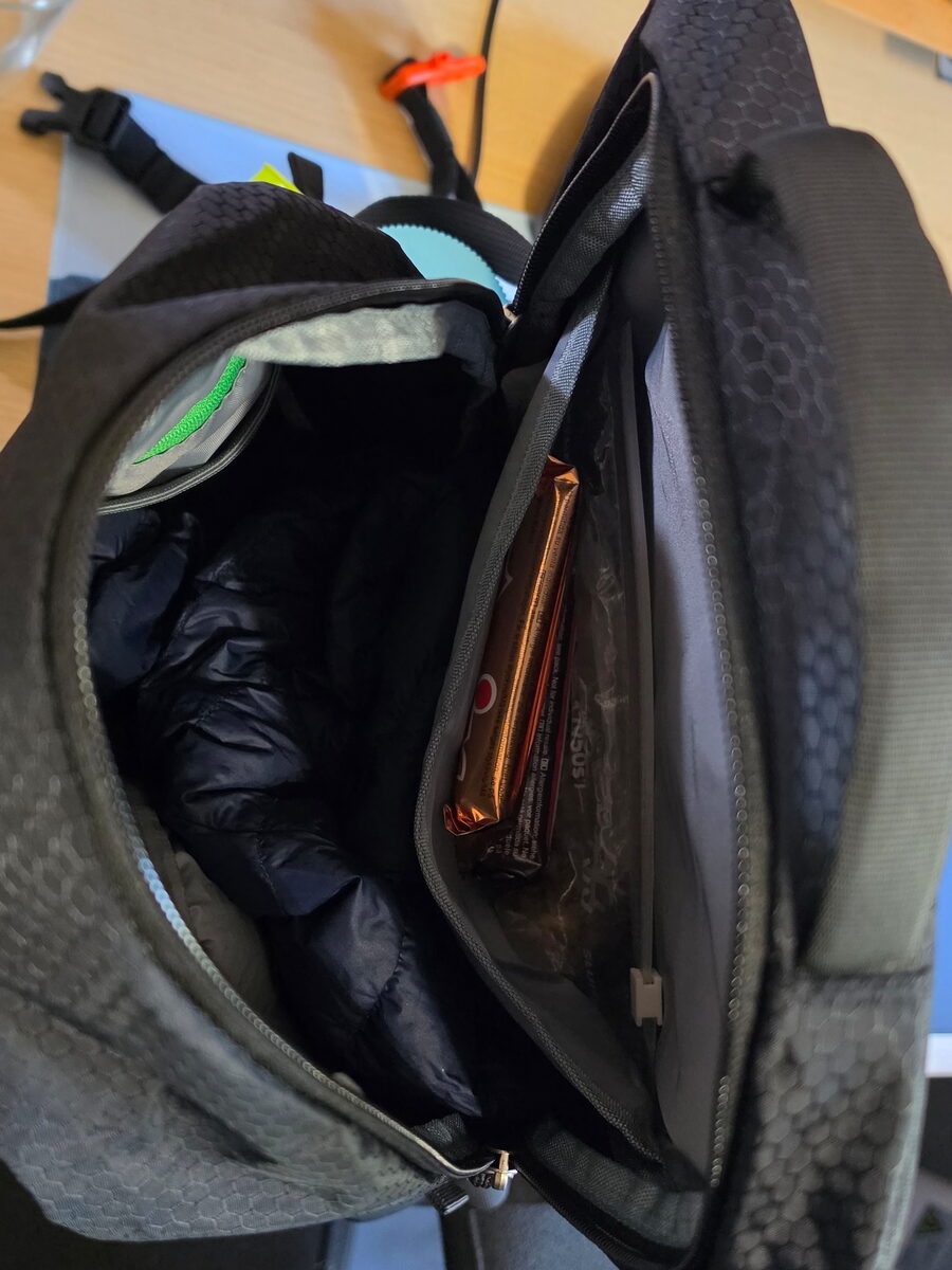 Open main compartment of the WATERFLY 20L with a down jacket and protein bars in an inner pocket